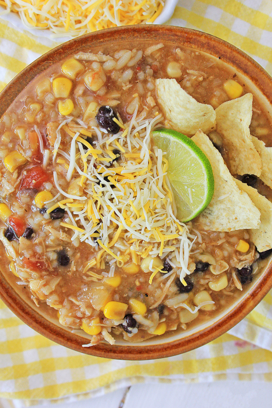 Instant Pot Mexican Chicken and Rice Soup served in a brown bowl, topped with lime slice, chips and shredded cheese