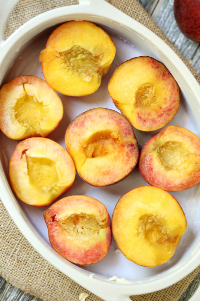 halves of peaches sitting in a baking white baking dish