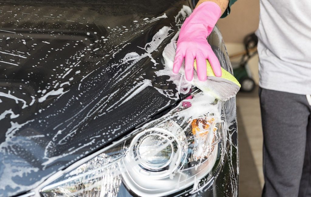 a person wearing a pink rubber glove washing the front of a car