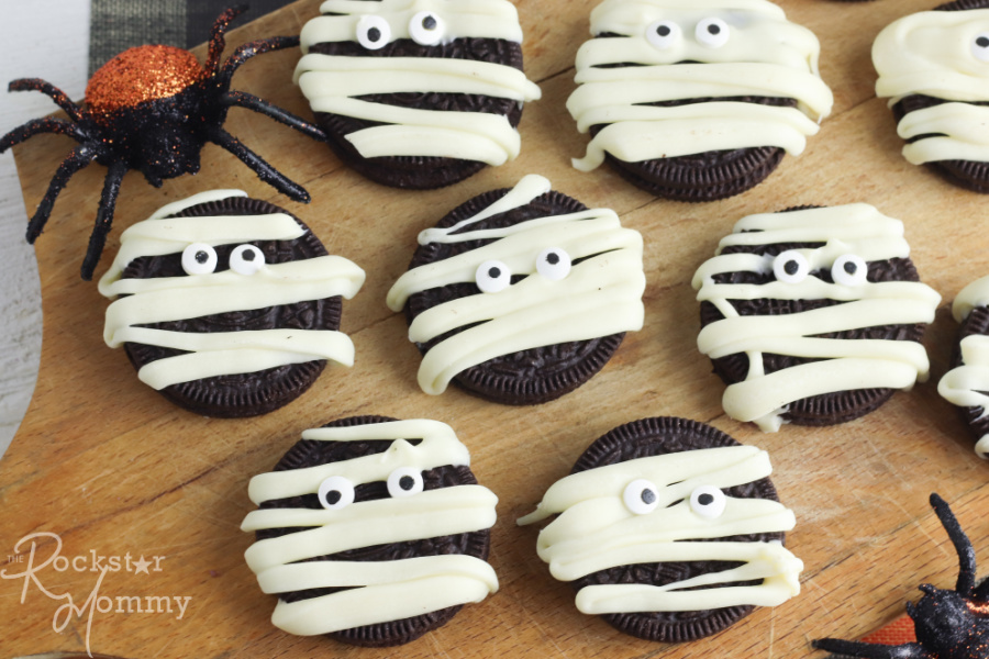 Mummy Oreo Cookies on a cutting board with 2 decorative spiders