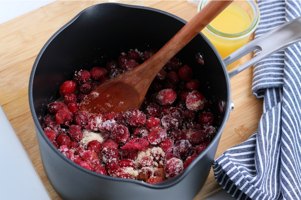 Cranberries, white and brown sugars, cinnamon and salt in a sauce pan with a wooden spoon