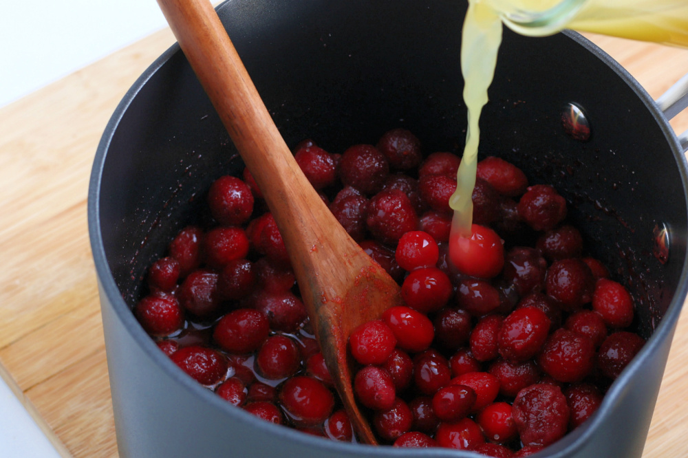 pouring orange juice in to sauce pan with cranberries