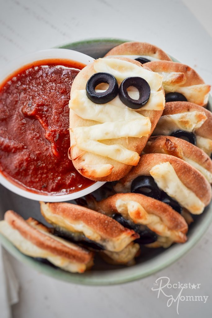 mini mummy pizzas stack in a bowl with red dipping sauce
