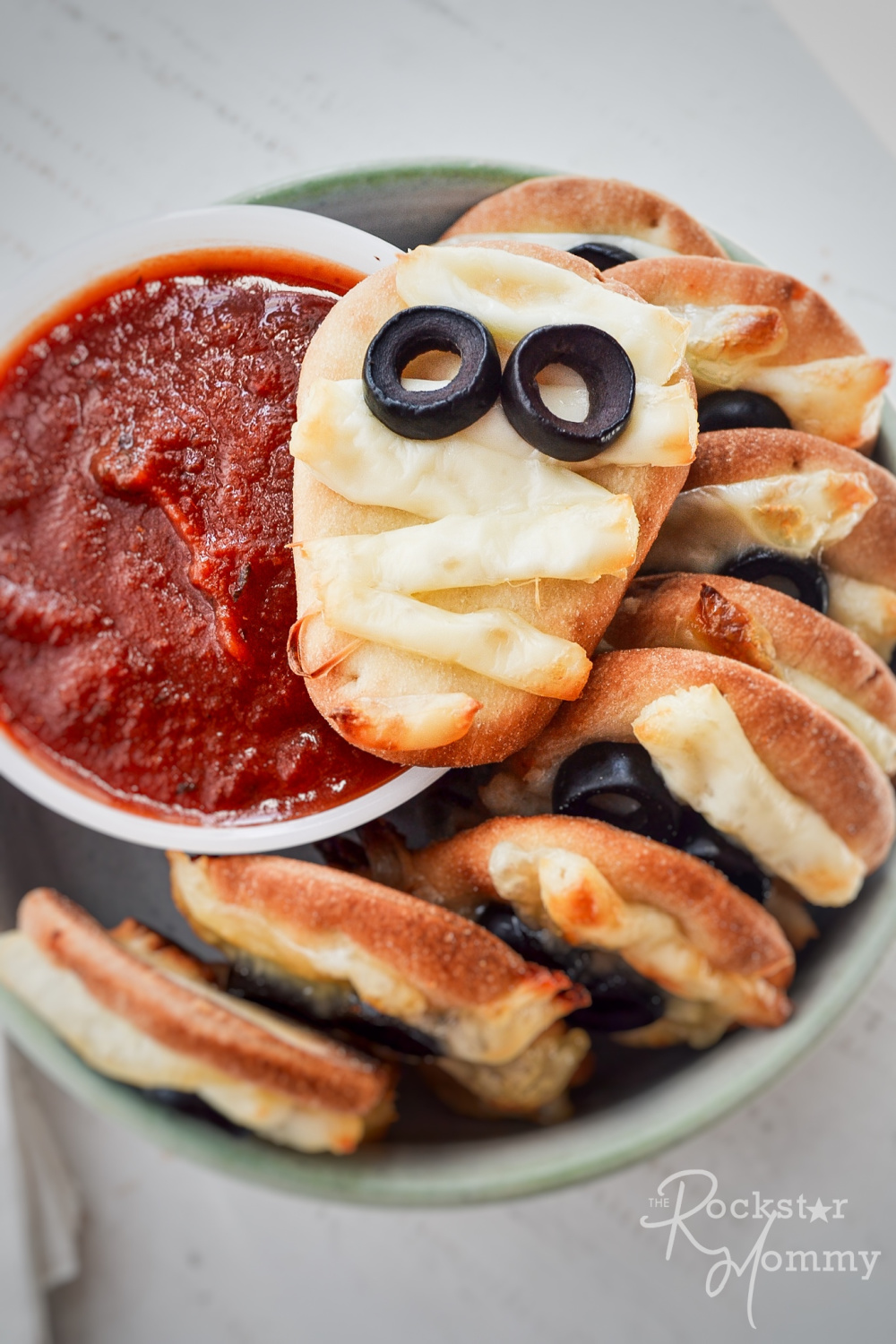 mini mummy pizzas stack in a bowl with red dipping sauce