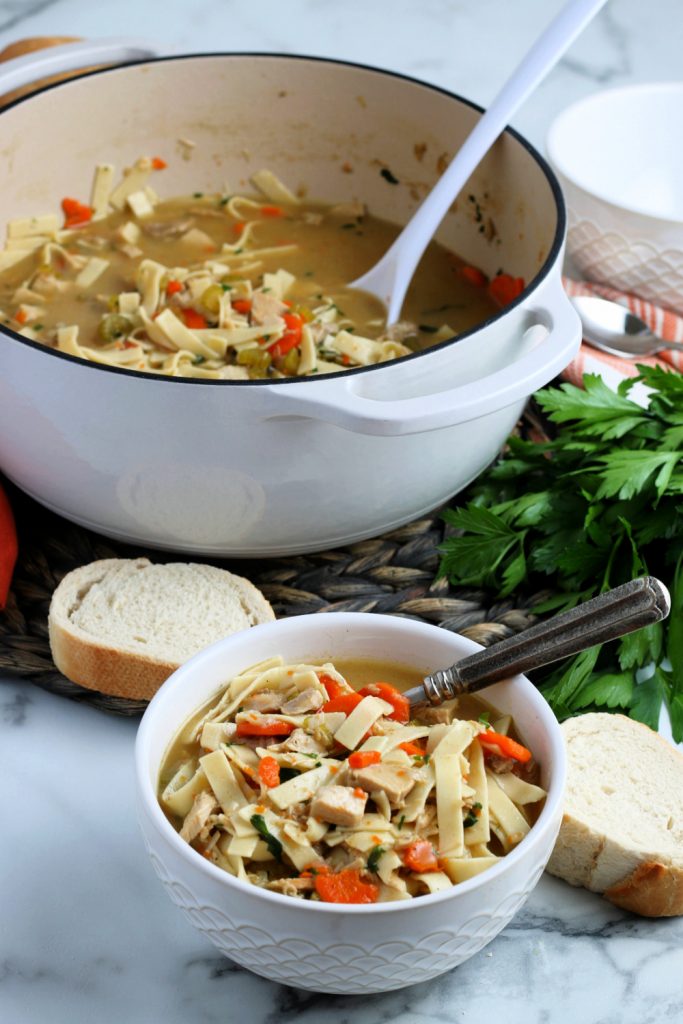 Turkey noodle soup being served in a bowl with some sliced bread