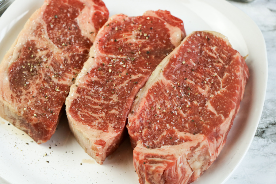three steaks on a white plate, seasoned with salt and pepper