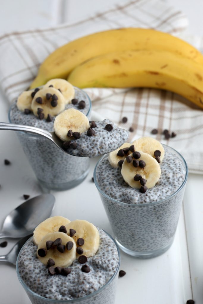 3 cups of chia pudding topped with sliced bananas and chocolate chips with a spoon scooping some up