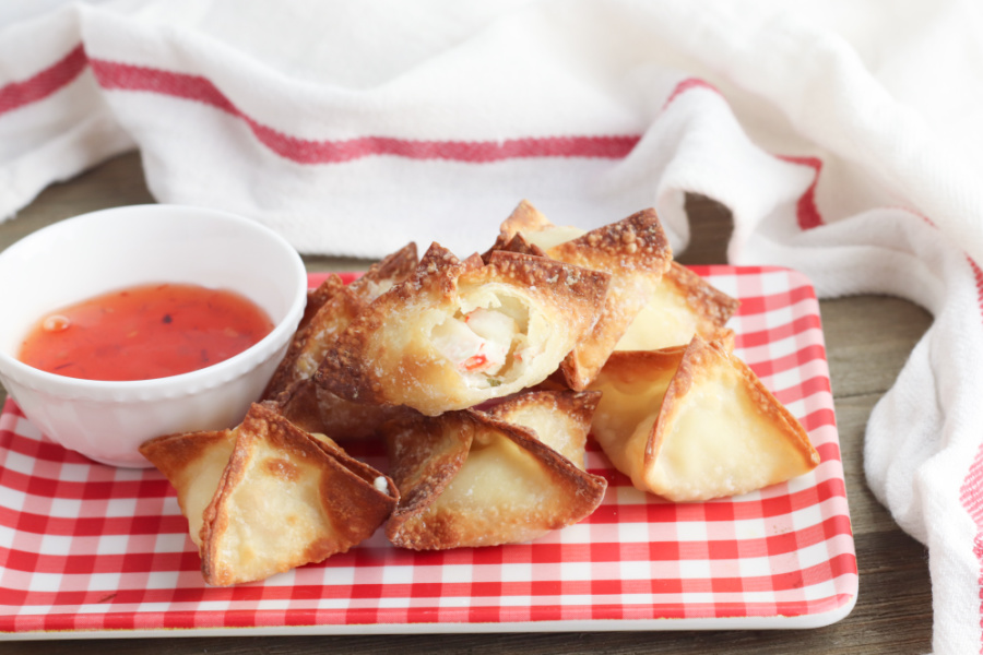 air fryer crab rangoons stacked on a plate with a small bowl of sauce