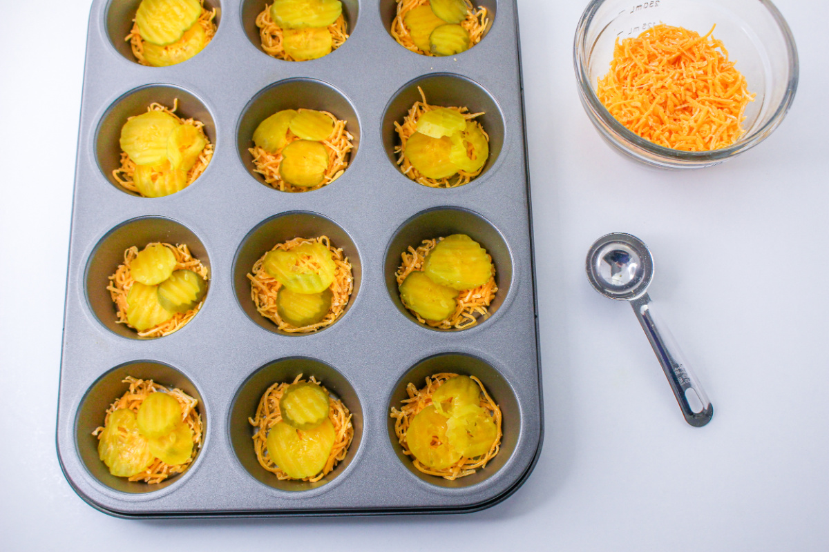 shredded cheese and pickle chips in muffin tin