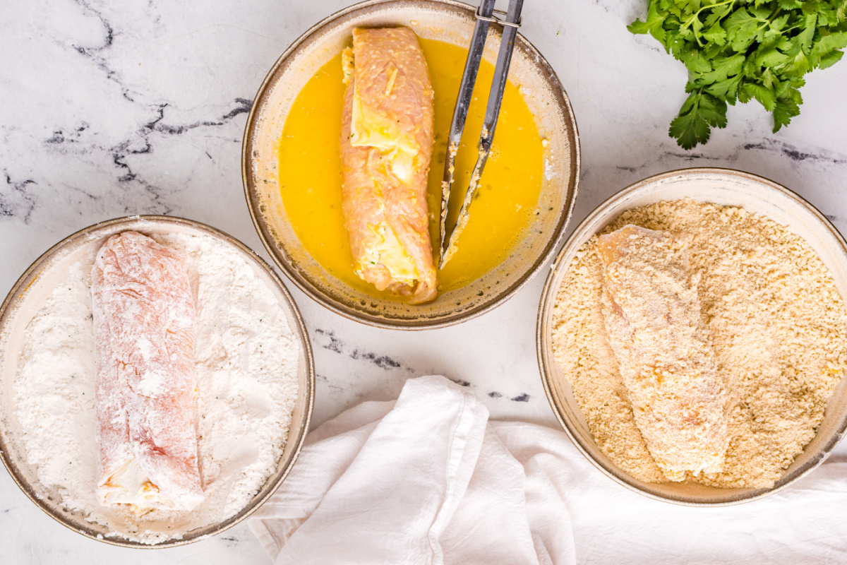 chicken rolls being dipped in flour, egg, and bread crumbs