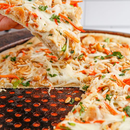 hand picking up a slice of Copycat California Pizza Kitchen Thai Chicken Pizza