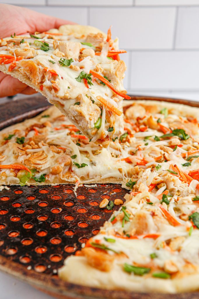 hand picking up a slice of Copycat California Pizza Kitchen Thai Chicken Pizza