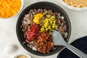 bacon, bread crumbs, mustard, ketchup, Worcestershire, pickles, and seasonings added to pan