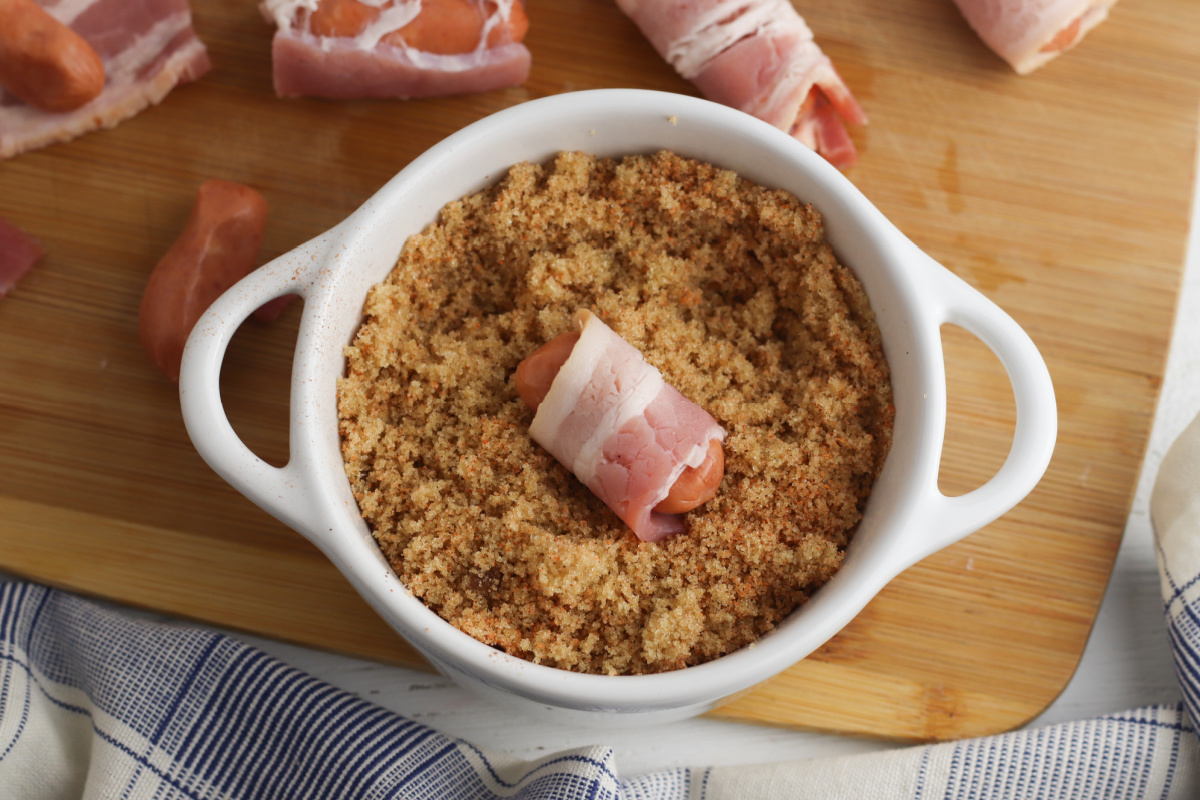 rolling bacon wrapped mini sausage in a bowl of brown sugar and cajun seasoning