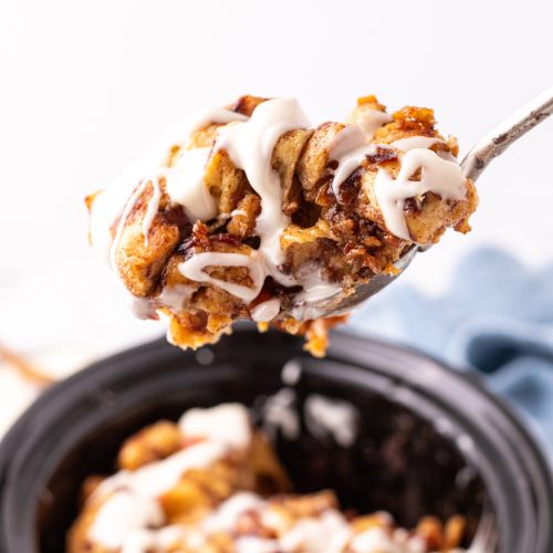 Slow Cooker Cinnamon Roll Casserole in a slow cooker with a serving spoon