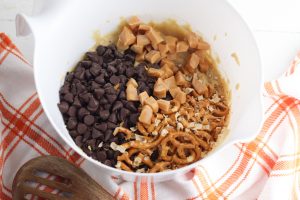 chocolate chips, caramel, and pretzels added to bowl