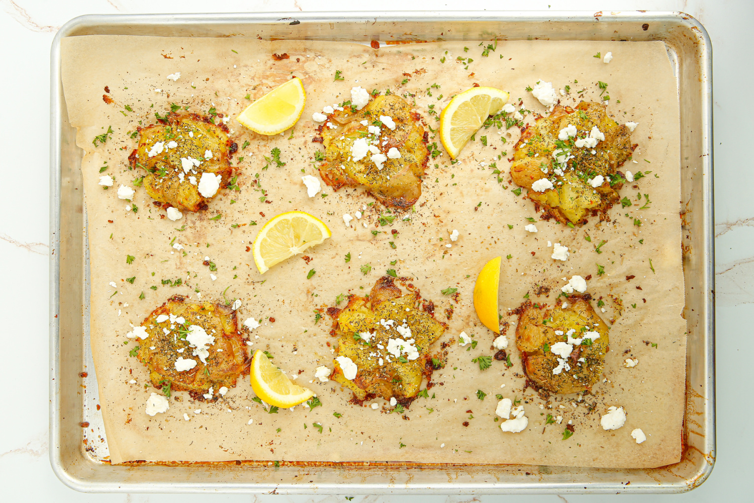 Crispy Greek Smashed Potatoes on a baking sheet with feta cheese and lemons